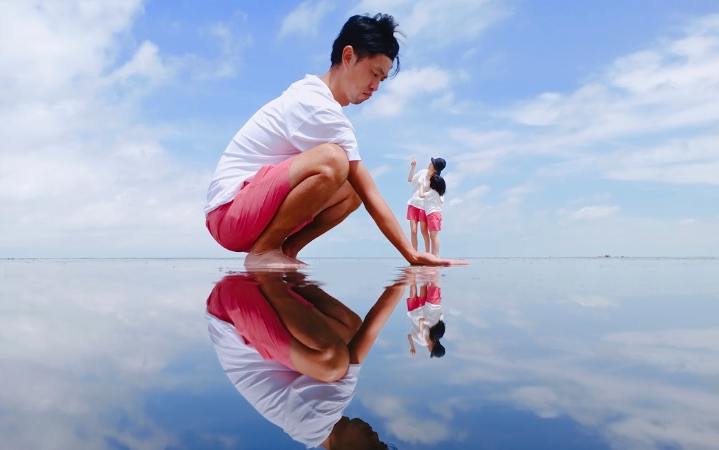 Man crouching on reflective water surface at Sky Mirror, Kuala Selangor.