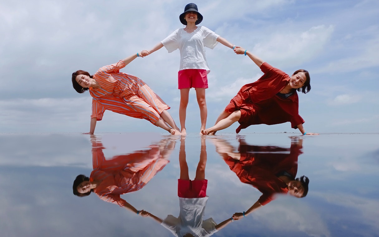 Three people posing on reflective water at Sky Mirror, Kuala Selangor.
