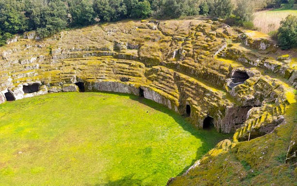 Ancient amphitheater ruins at Sutri Pass, Italy, surrounded by greenery.