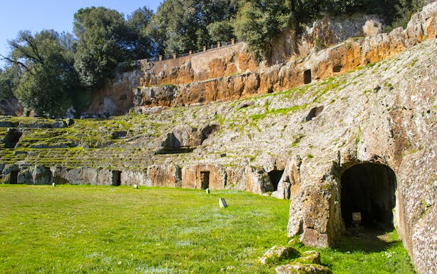 Ancient amphitheater carved into rock at Sutri Pass, Italy, surrounded by greenery.