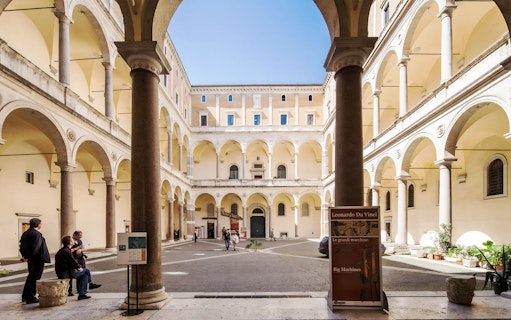 Courtyard of Palazzo della Cancelleria in Rome, featuring a Leonardo da Vinci exhibition sign.