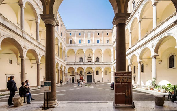 Courtyard of Palazzo della Cancelleria in Rome, featuring a Leonardo da Vinci exhibition sign.
