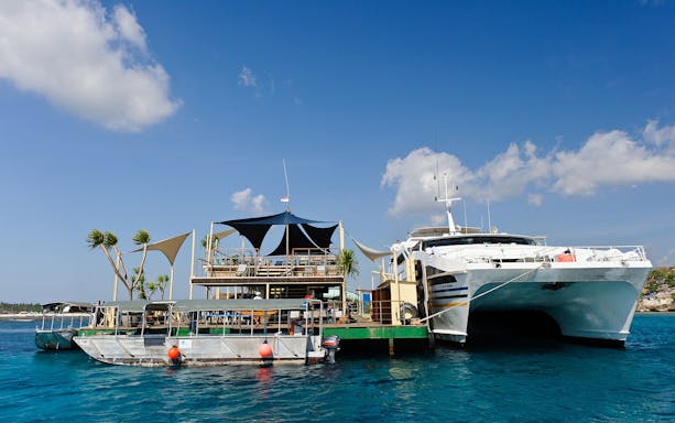Catamaran docked at Nusa Lembongan Island with floating platform and clear blue sky.