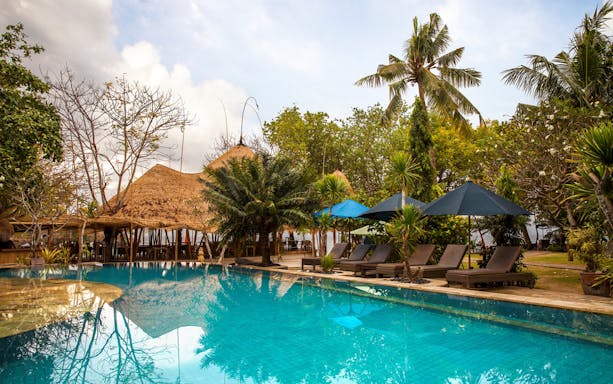 Poolside view with lounge chairs and tropical huts on Nusa Lembongan Island.