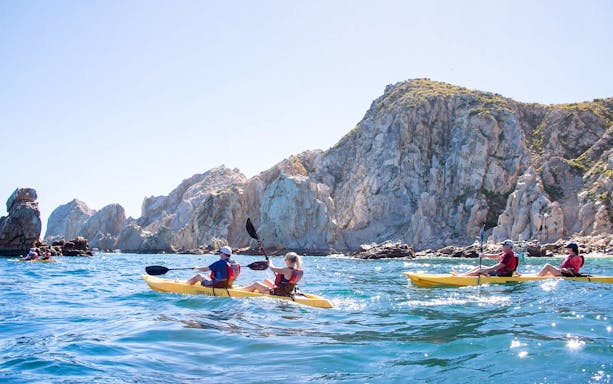 Kayakers paddling near rocky cliffs in Cabo San Lucas.