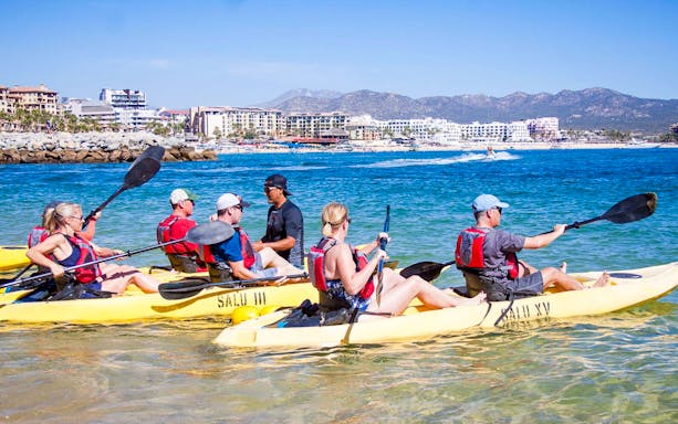 Kayakers in Cabo San Lucas with cityscape and mountains in the background.