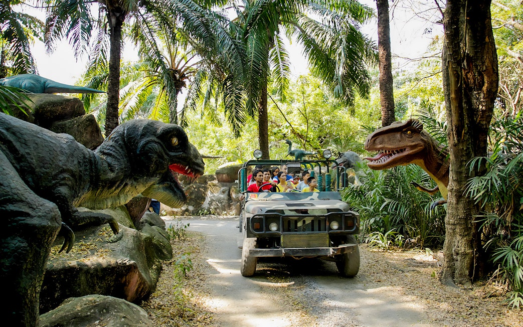 Visitors on a safari jeep tour at Siam Amazing Park, surrounded by dinosaur sculptures.