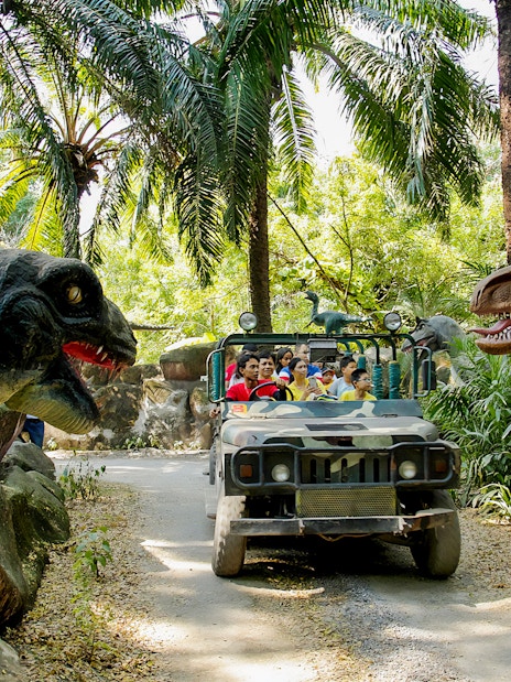 Visitors on a safari jeep tour at Siam Amazing Park, surrounded by dinosaur sculptures.