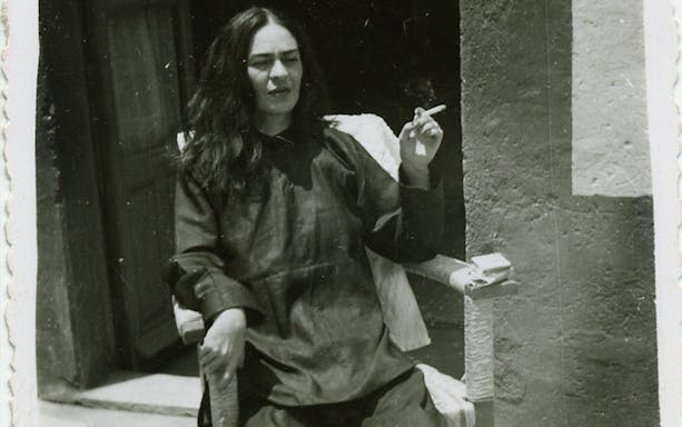 Frida Kahlo sitting outdoors, smoking, at Palais Galliera exhibition.