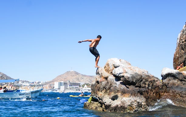 Man cliff jumping near paddleboarders at Cabo San Lucas Arch, Mexico.