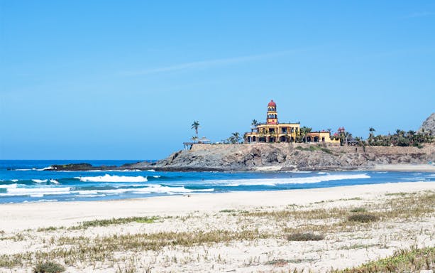 Todos Santos beach with historic building on rocky shore, Baja California Sur.
