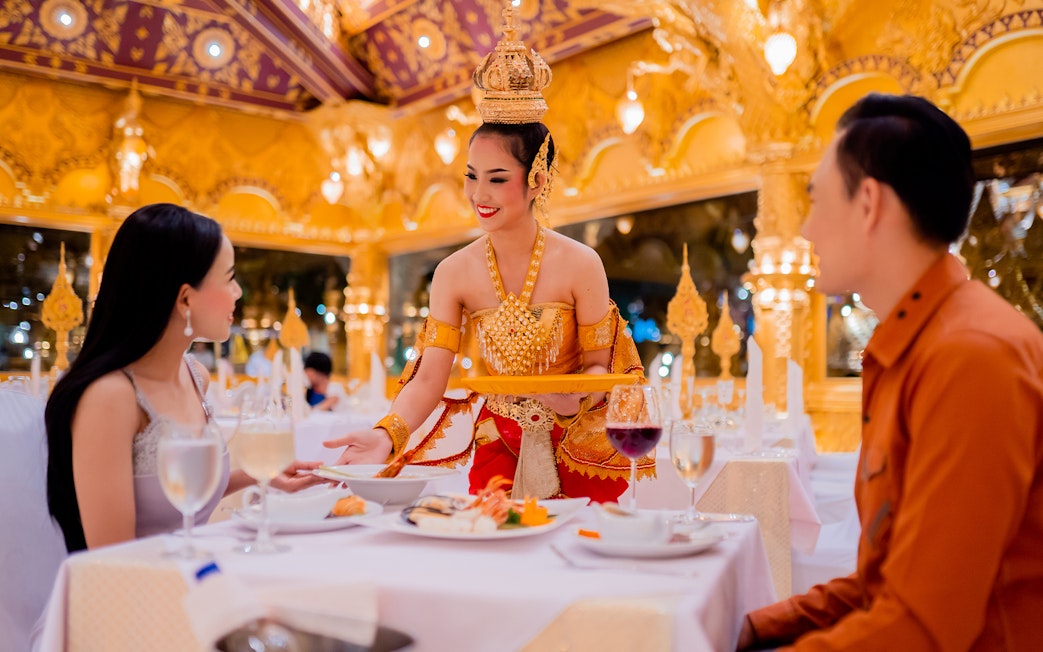 Server in traditional attire serving guests at Phuket Fantasea dinner show.