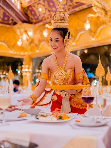 Server in traditional attire serving guests at Phuket Fantasea dinner show.