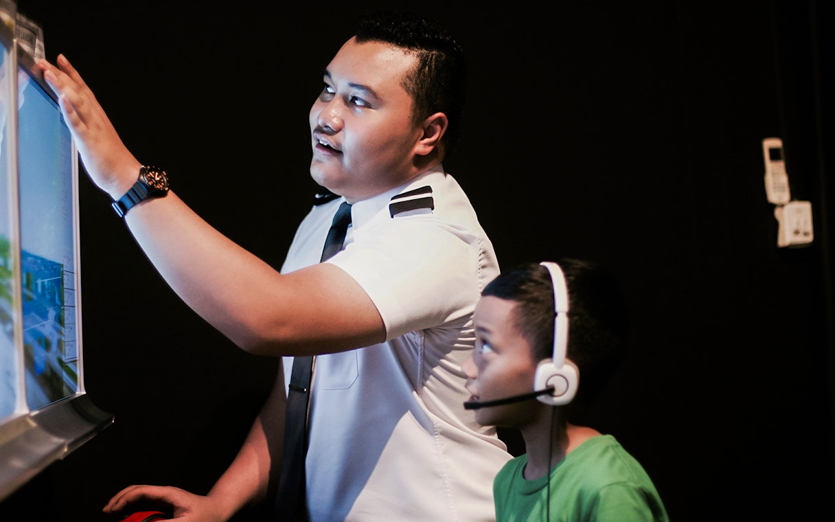 Pilot guiding child in flight simulator during Aeroviation Full Flight Experience.