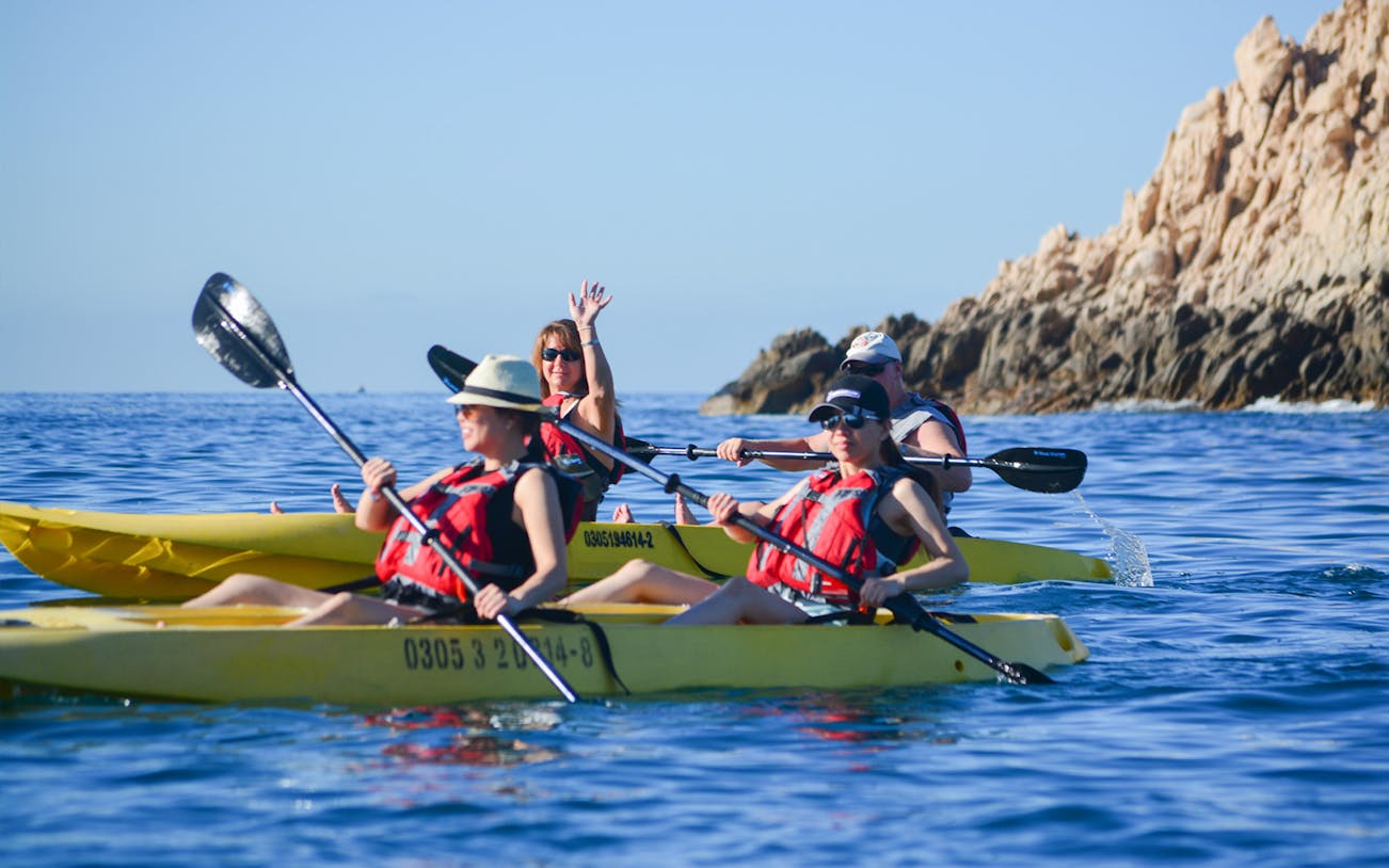 Kayakers in glass bottom kayaks near rocky cliffs on Cabo San Lucas tour.