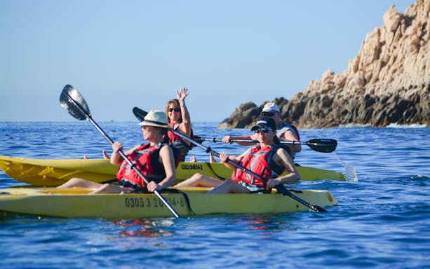 Kayakers in glass bottom kayaks near rocky cliffs on Cabo San Lucas tour.