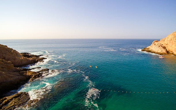 Glass bottom kayaks on clear waters near rocky coastline in Cabo San Lucas.