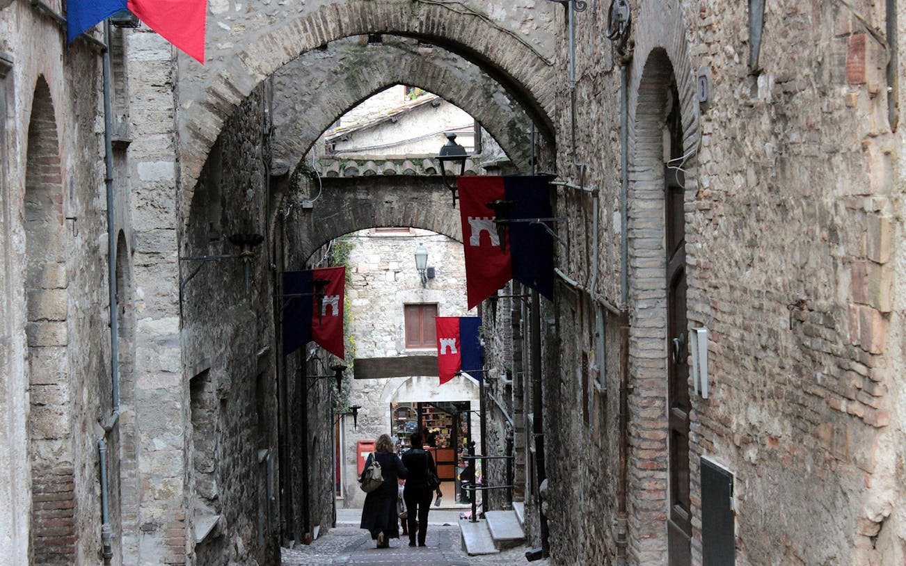 Narrow stone alley with arches and flags in Narni, Italy.