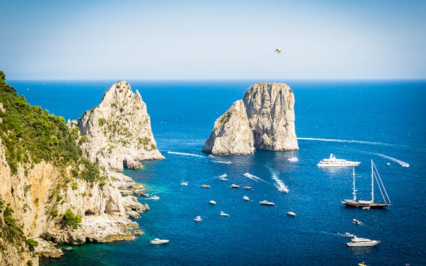 Boats near Faraglioni rock formations in Capri, Italy, with clear blue sea and sky.