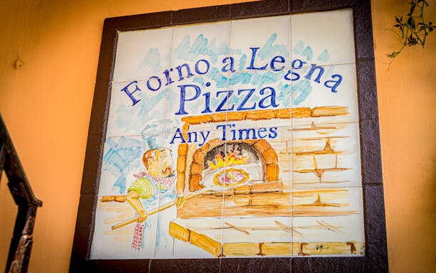 Wood-fired pizza sign in Capri, Italy, depicting a chef placing pizza in an oven.