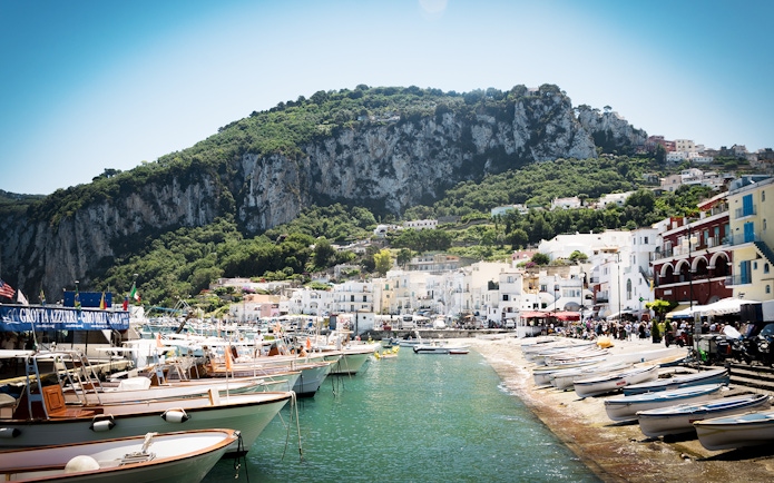 Boats docked at Marina Grande, Capri with cliffs and hillside buildings in the background.