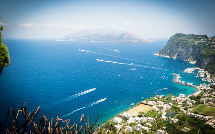 Aerial view of Capri coastline with boats in the sea, showcasing lush cliffs and marina.