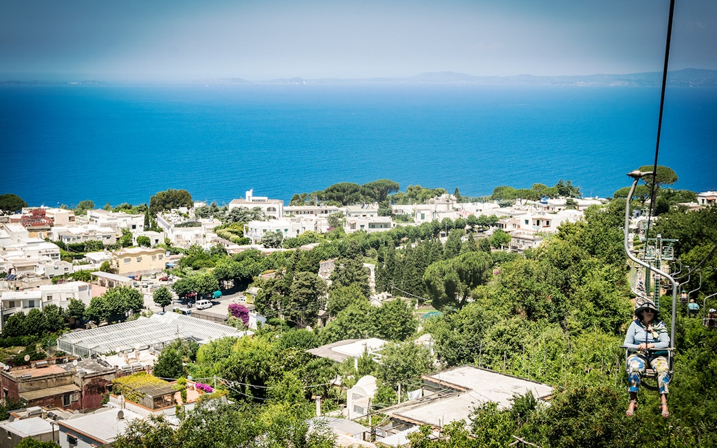 Chairlift view over Anacapri with lush greenery and the sea, part of Capri & Anacapri tour from Sorrento.