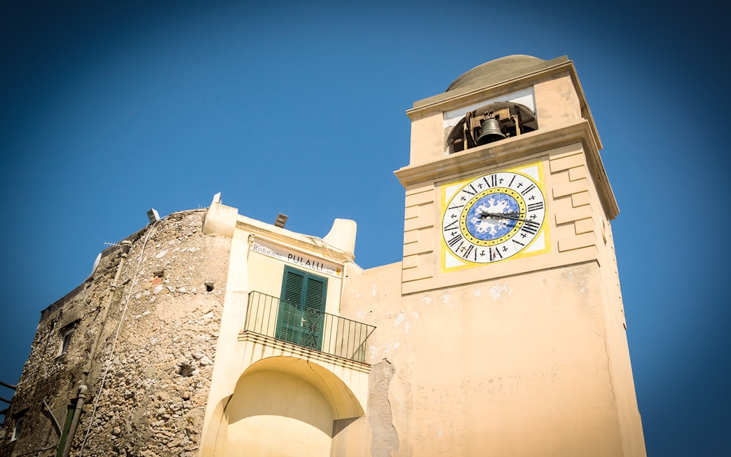 Clock tower in Capri, Italy, with Roman numerals and bell, part of Capri & Anacapri tour.