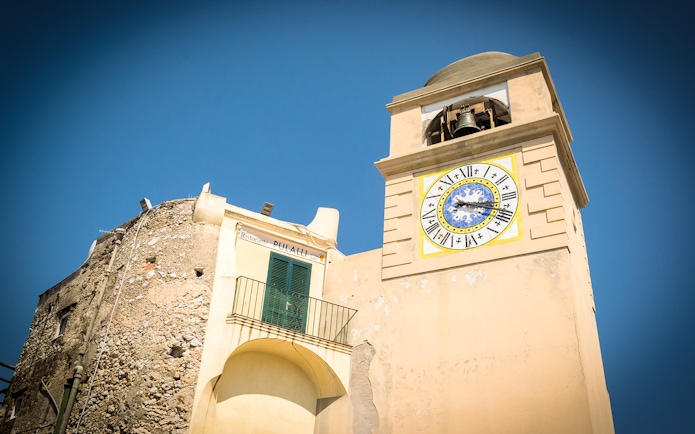 Clock tower in Capri, Italy, with Roman numerals and bell, part of Capri & Anacapri tour.