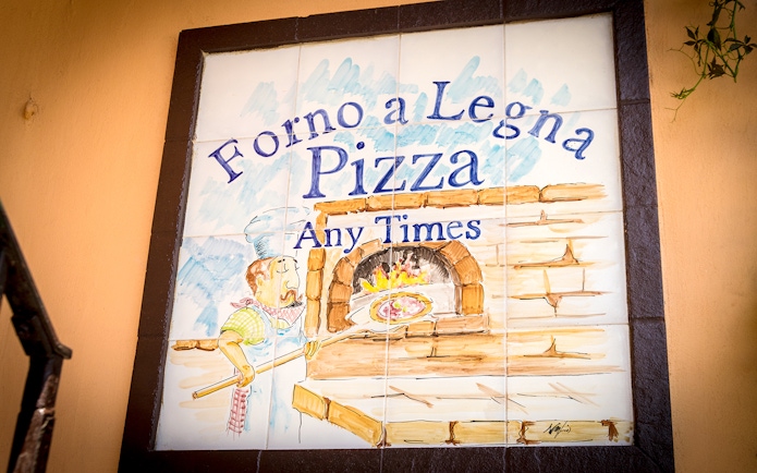 Wood-fired pizza oven sign in Capri, Italy, featuring a chef with a pizza paddle.