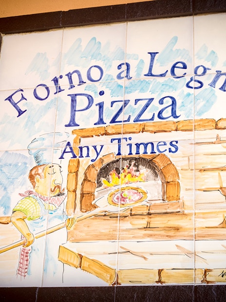 Wood-fired pizza oven sign in Capri, Italy, featuring a chef with a pizza paddle.