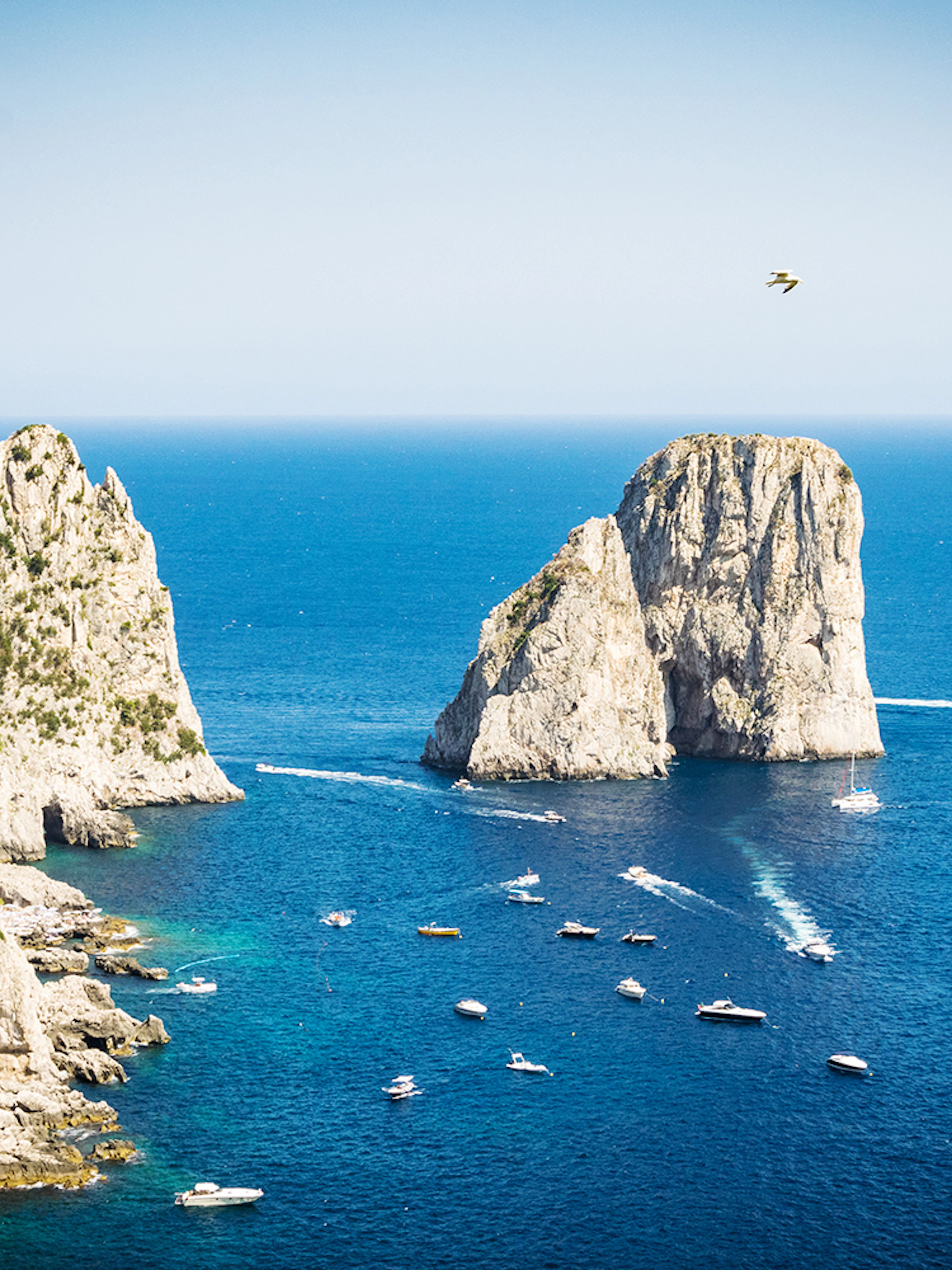 Boats near Faraglioni rock formations in Capri, Italy, viewed from the sea.