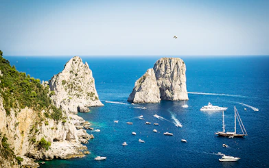 Boats near Faraglioni rock formations in Capri, Italy, viewed from the sea.