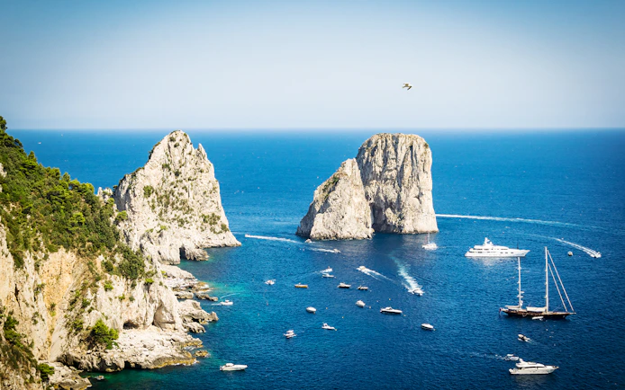Boats near Faraglioni rock formations in Capri, Italy, viewed from the sea.