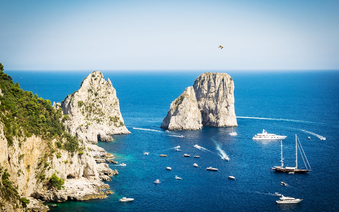 Boats near Faraglioni rock formations in Capri, Italy, viewed from the sea.