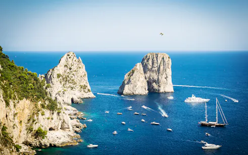 Boats near Faraglioni rock formations in Capri, Italy, viewed from the sea.