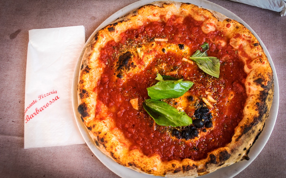 Pizza with tomato sauce and basil leaves on a plate, served at a Naples pizzeria.