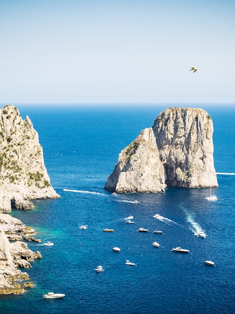 Boats near Faraglioni rock formations on Capri Island, Italy, with clear blue sea.