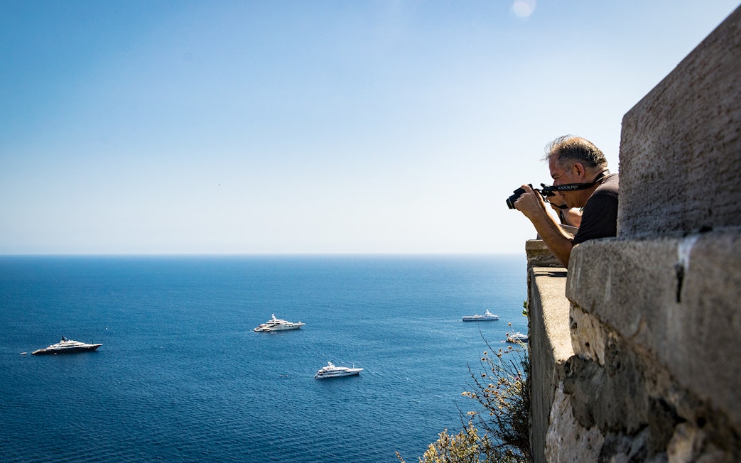Photographer capturing yachts on the sea from a cliff on Capri Island.