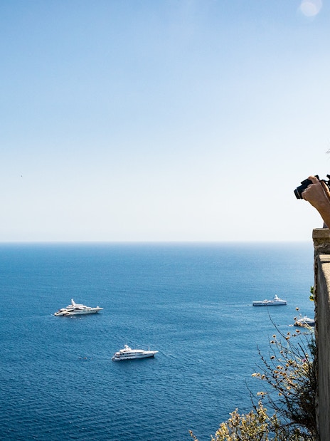 Photographer capturing yachts on the sea from a cliff on Capri Island.