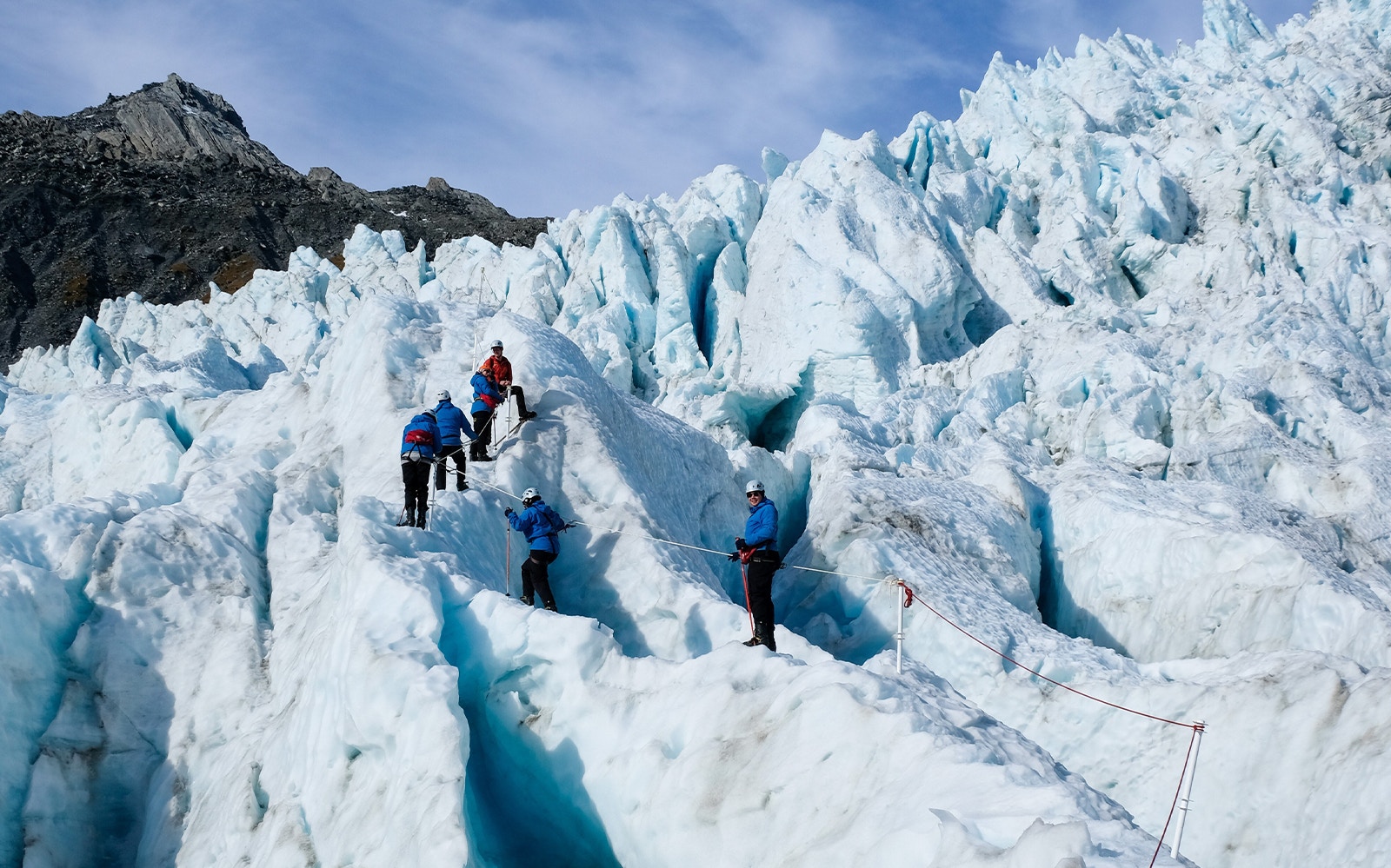 Group hiking on Franz Josef Glacier with ropes and gear.