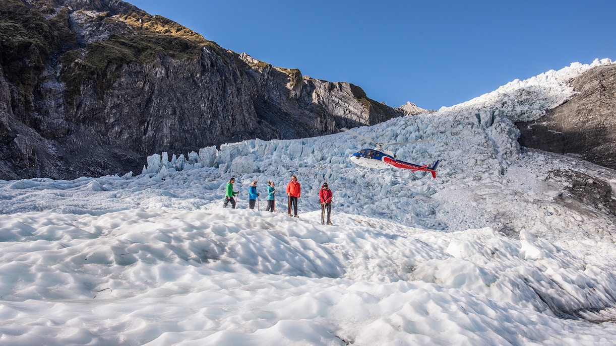 Group hiking on Franz Josef Glacier with helicopter in background.