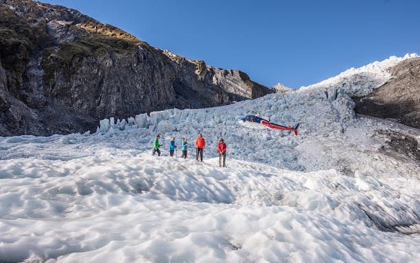 Group hiking on Franz Josef Glacier with helicopter in background.