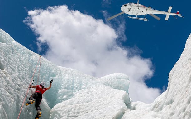 Climber ascending ice wall with helicopter above at Franz Josef Glacier.