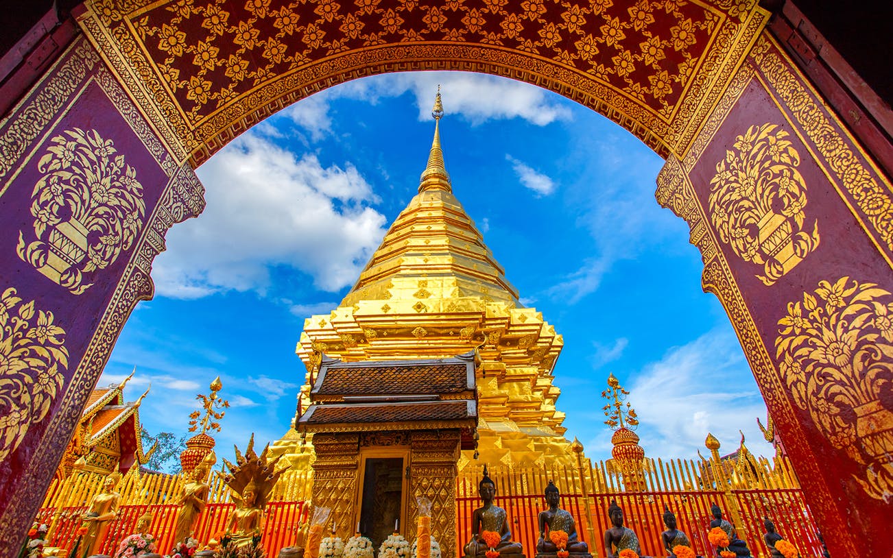 Golden stupa at Wat Phra That Doi Suthep, Chiang Mai, viewed through ornate archway.
