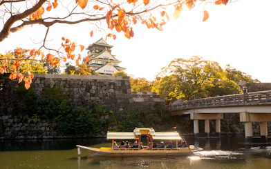 Osaka Castle with boat on moat under autumn leaves.