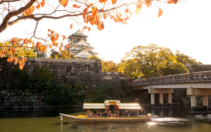 Osaka Castle with boat on moat under autumn leaves.