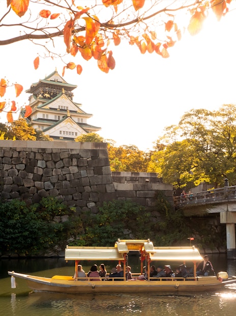 Osaka Castle with boat on moat under autumn leaves.