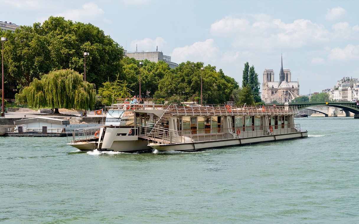 Seine River cruise boat with Notre-Dame Cathedral in the background, Paris.