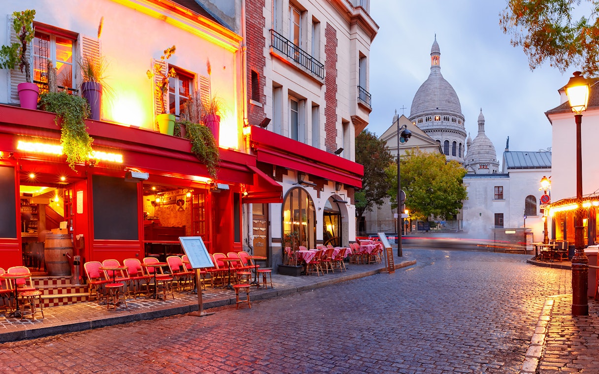 Montmartre street with Sacré-Cœur Basilica in Paris, featuring outdoor café seating.